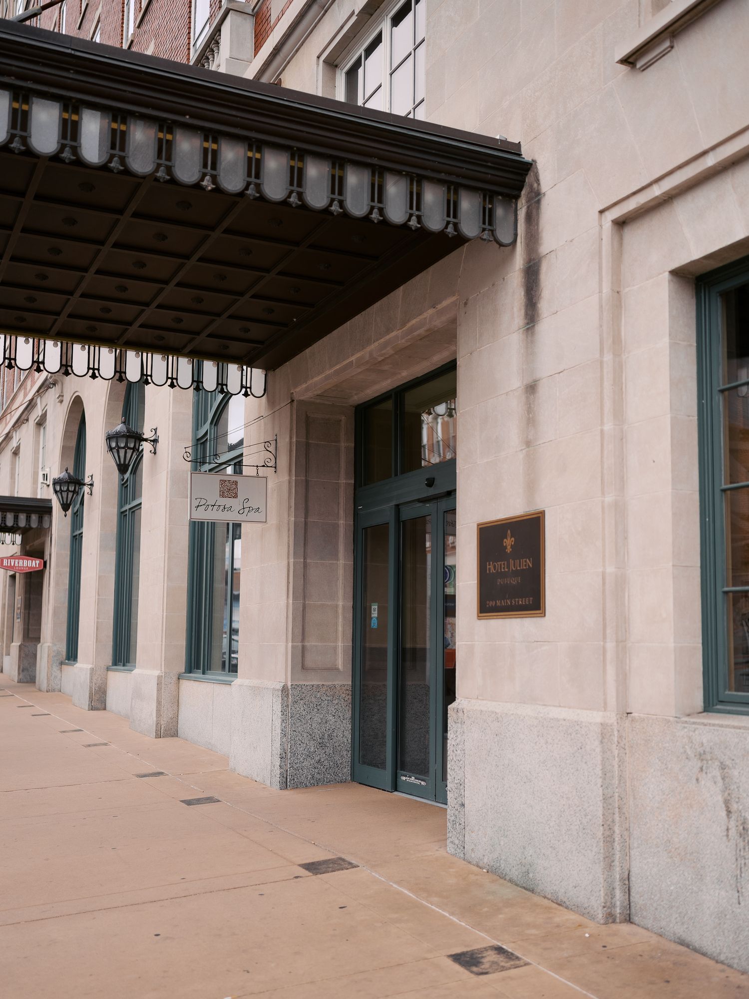 Vintage scalloped awning extends over a stone building entrance with antique wall-mounted lamp and brass plaque.