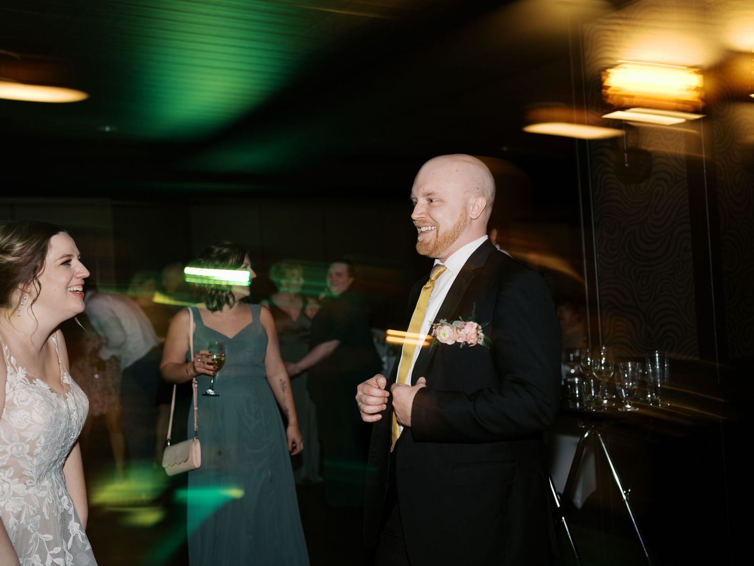 Guests dancing and celebrating at a dimly lit wedding reception with green lighting effects in the background.