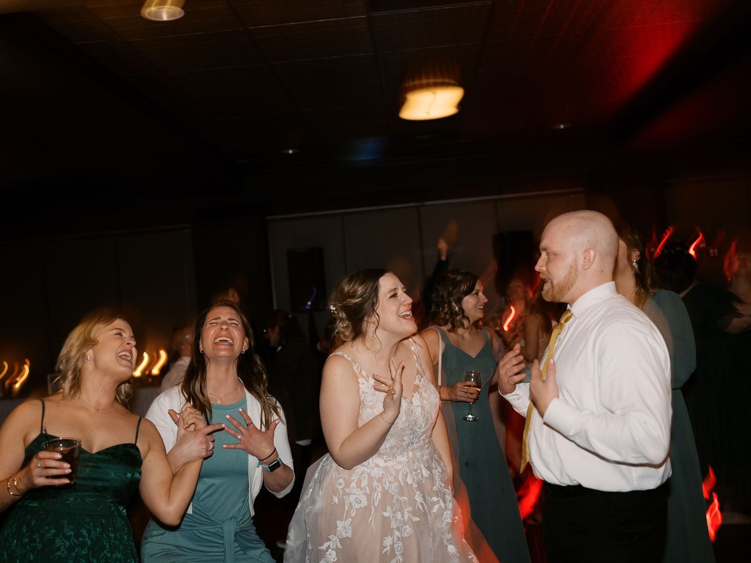 Wedding guests dancing and celebrating on a dimly lit dance floor at a reception party.