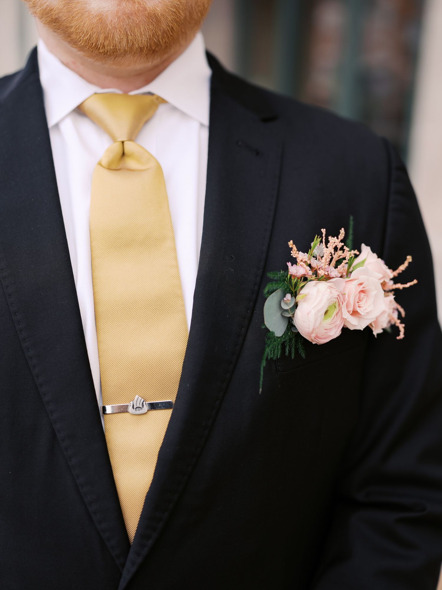 Close up of formal black suit with gold necktie and delicate pink floral boutonniere on lapel.