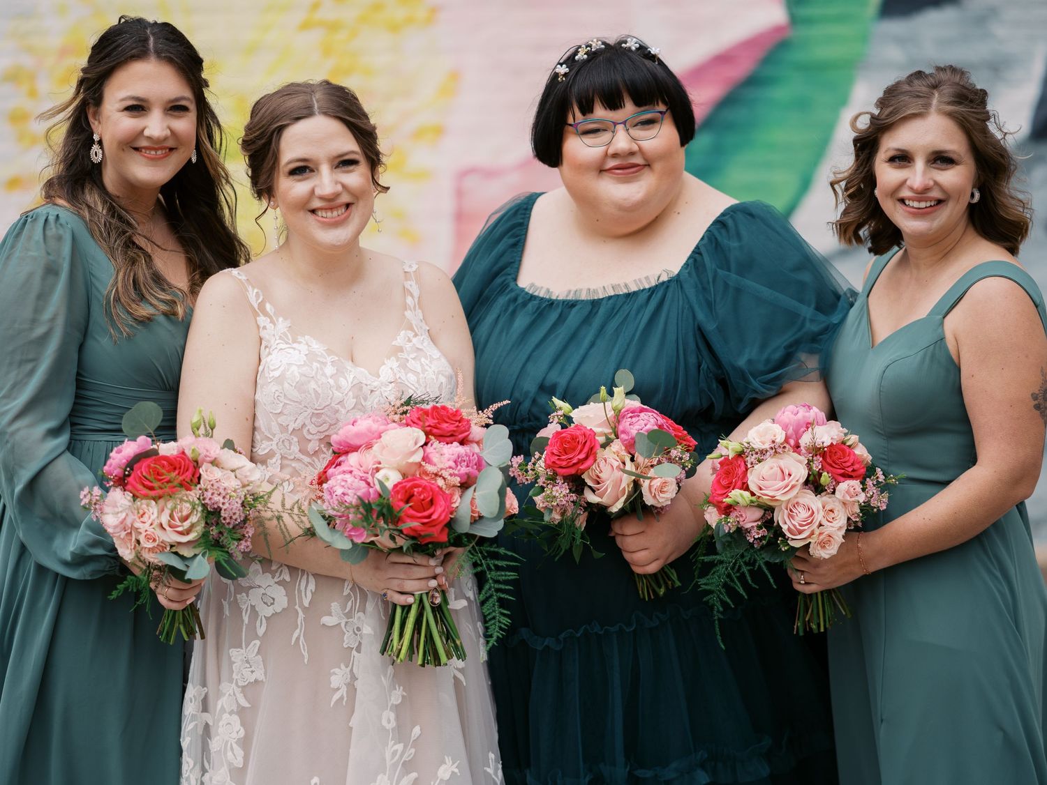 Wedding party wearing green bridesmaid dresses and lace gown holding pink and coral flower bouquets.