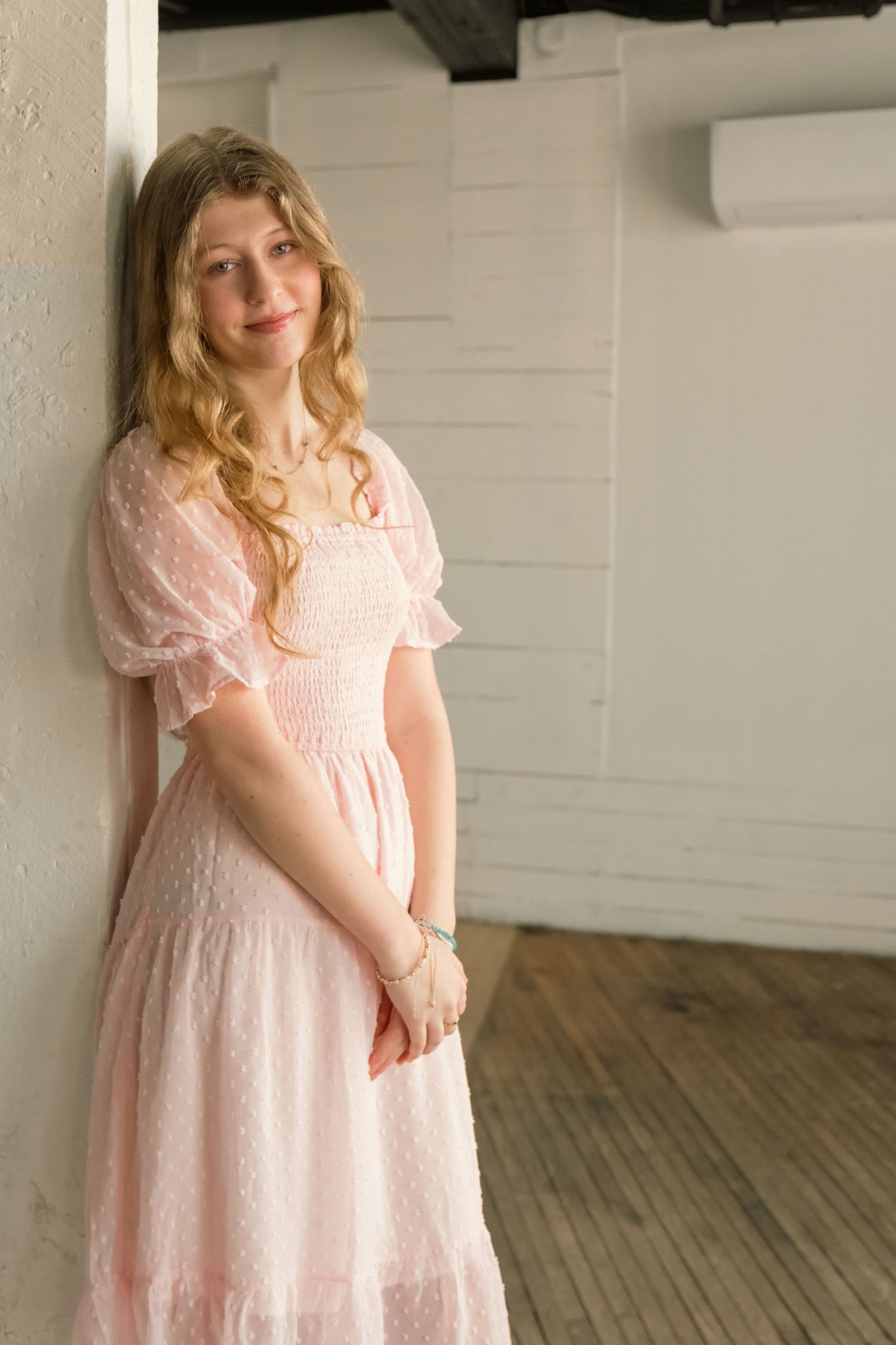 Someone wearing a romantic pink lace dress with puff sleeves stands near a white wall in a room with hardwood floors.