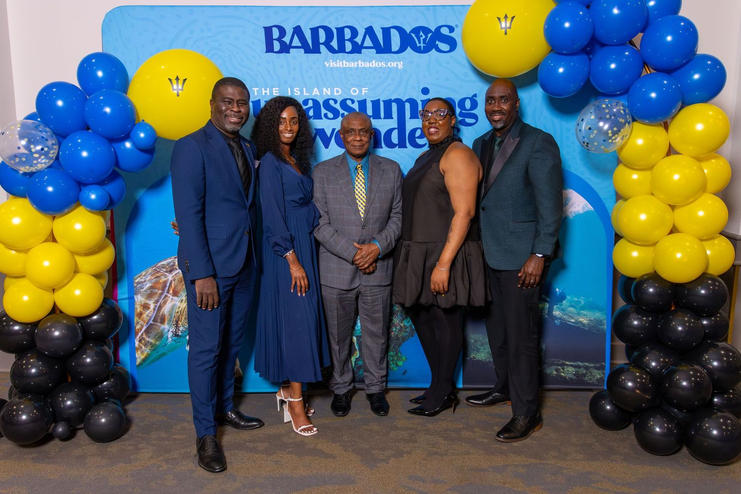 Event backdrop with blue and yellow balloon decorations and Barbados branding where attendees pose against the wall.