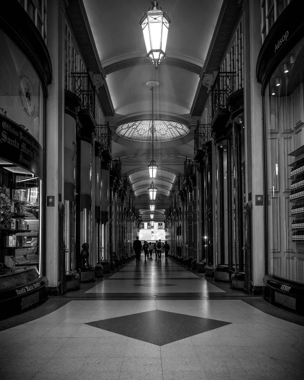 Elegant historic shopping arcade interior with arched ceiling and hanging lanterns illuminating a long corridor.