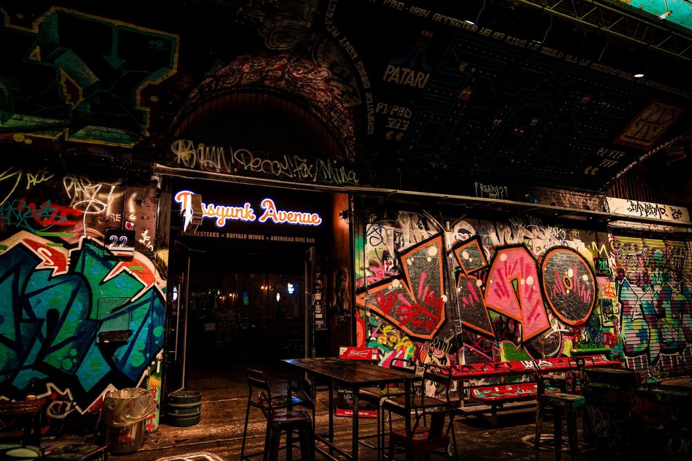 Five interconnected graffiti-covered walls in an urban tunnel create a colorful nighttime display with vibrant street art.