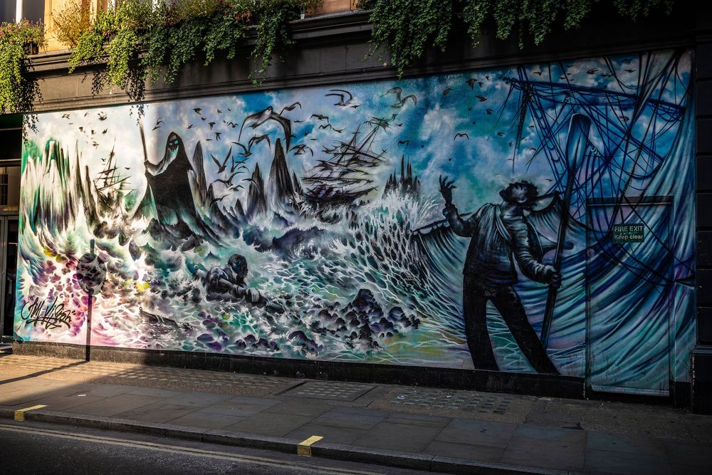 Colorful graffiti art murals cover a series of outdoor walls along an urban walkway or alley.