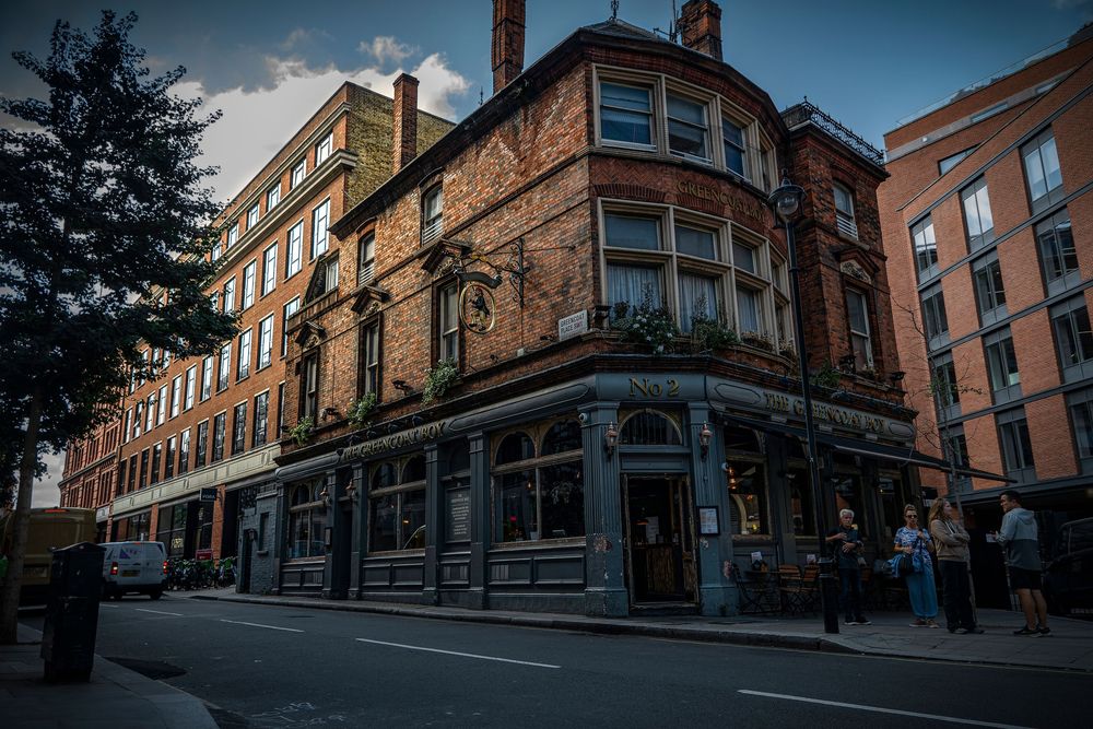 A row of historic brick buildings lines a cobblestone street in Glasgow's Merchant City district during twilight.