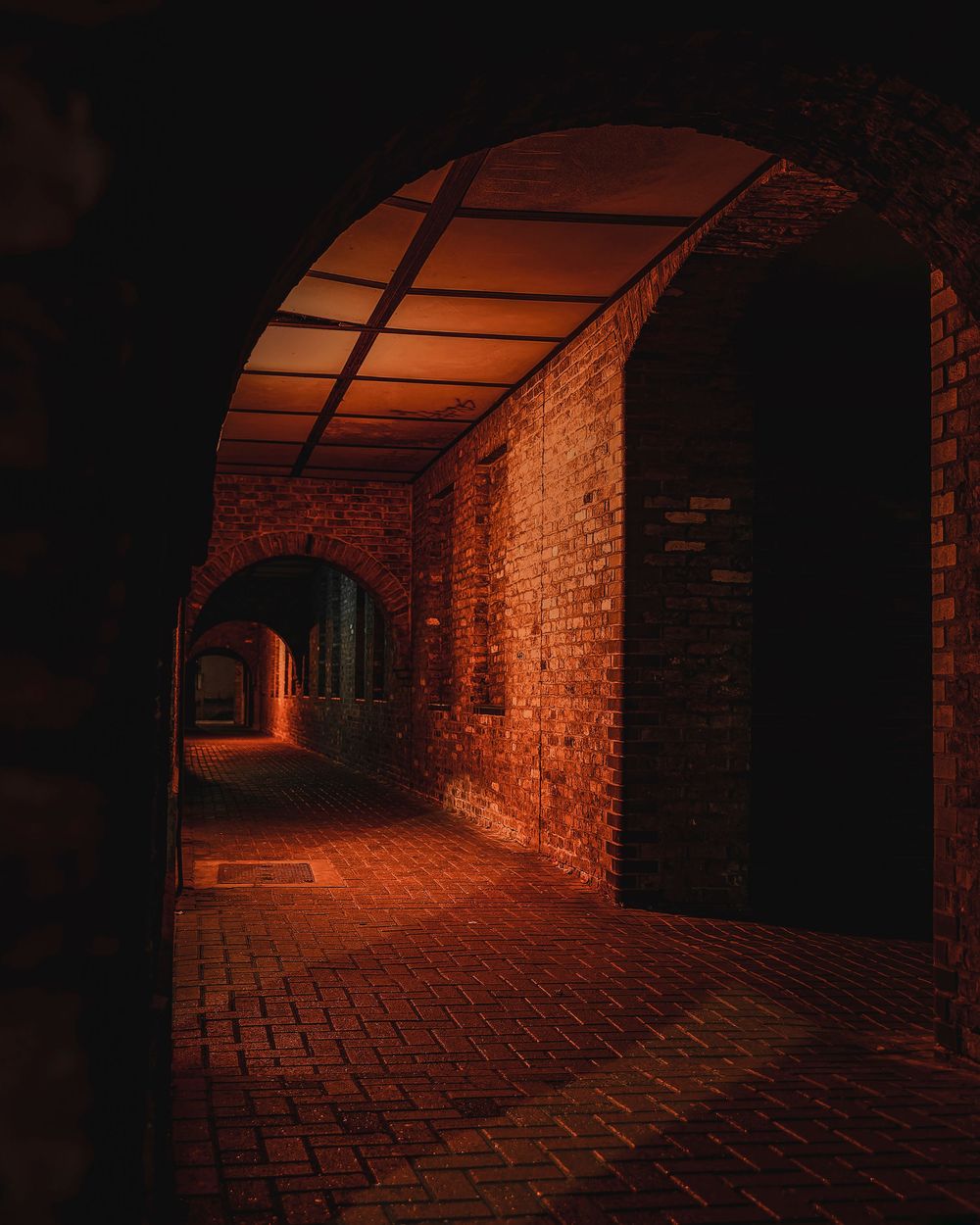 Dark underground brick tunnel illuminated with warm orange lighting creates an eerie atmosphere.