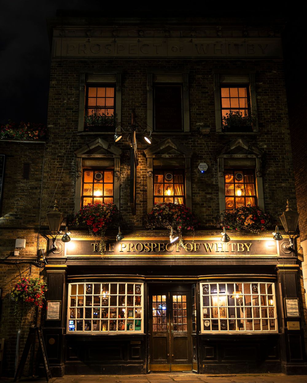 A cozy historic pub exterior with illuminated windows glows warmly at night on a stone building facade.