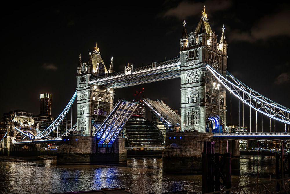 London's Tower Bridge illuminated at night with blue lights reflecting on the River Thames creating a dramatic cityscape.