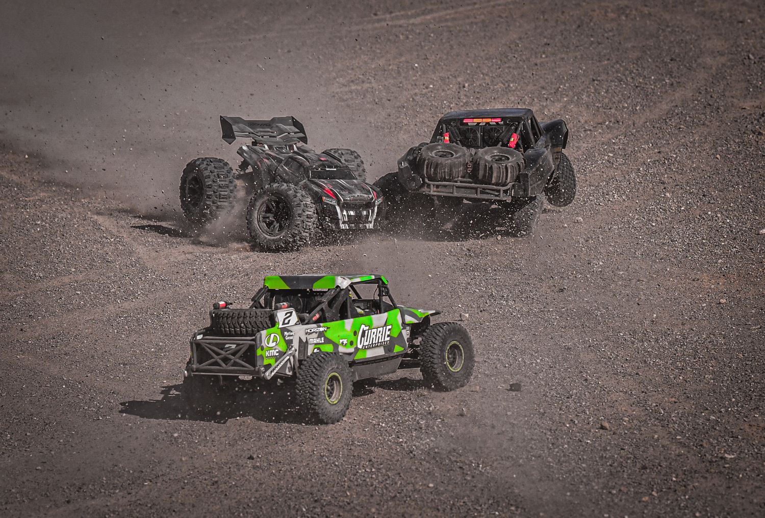 Green and black RC cars performing stunts and jumps on rugged terrain.