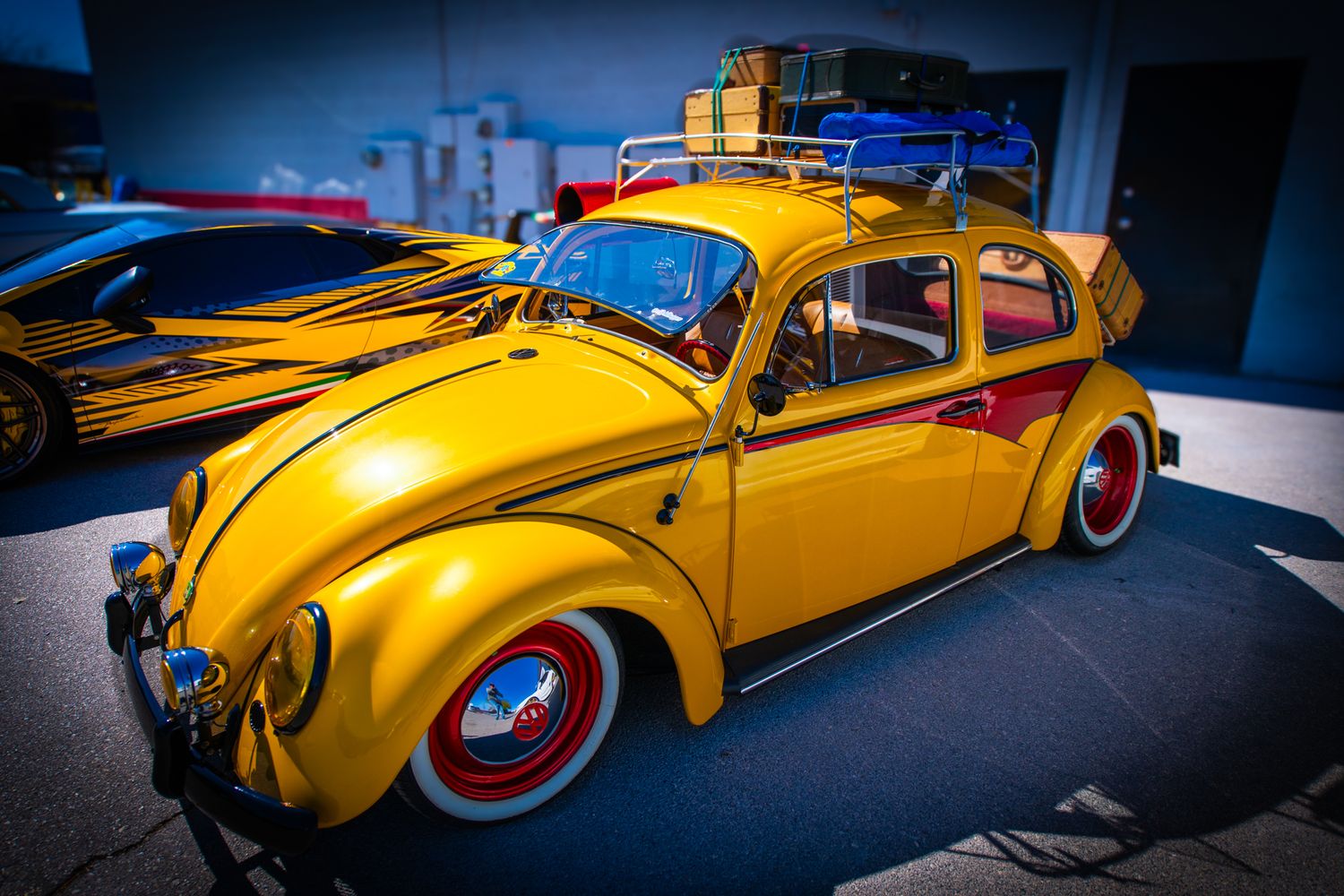 A customized yellow Volkswagen Beetle with red wheels displayed at a car show.