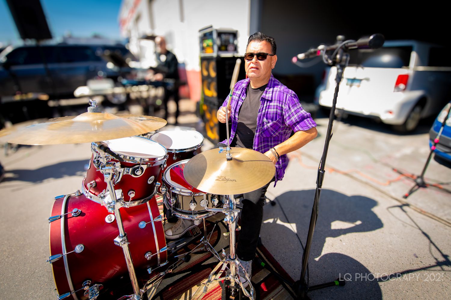 Drummer performing on a red drum kit at an outdoor event.