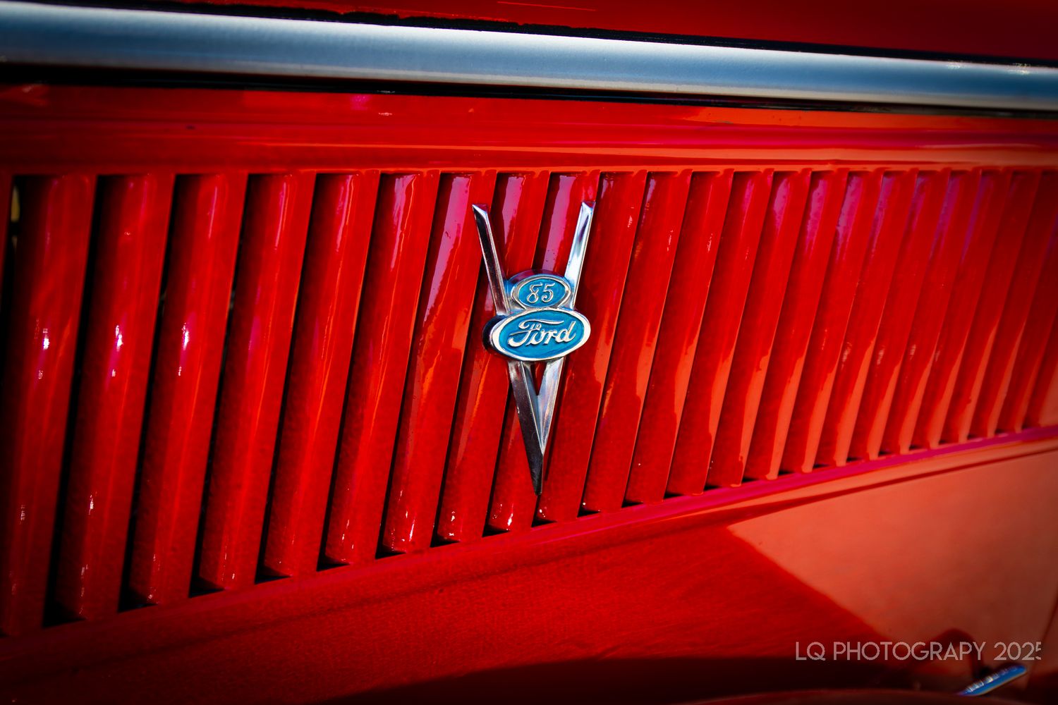 Close-up of a red vintage Ford grille with chrome V8 emblem.
