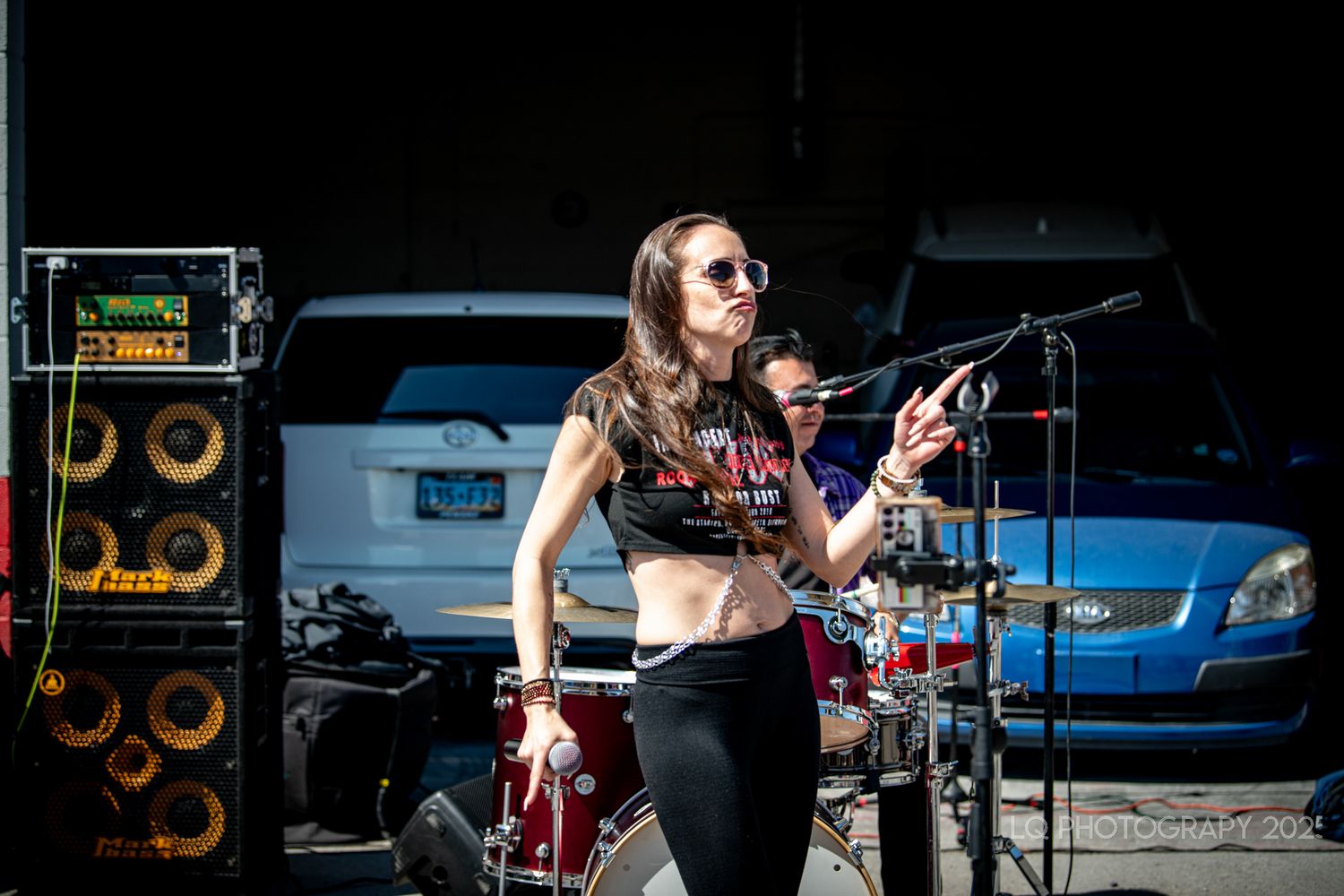 Female performer singing into microphone at outdoor concert with amp stack visible.