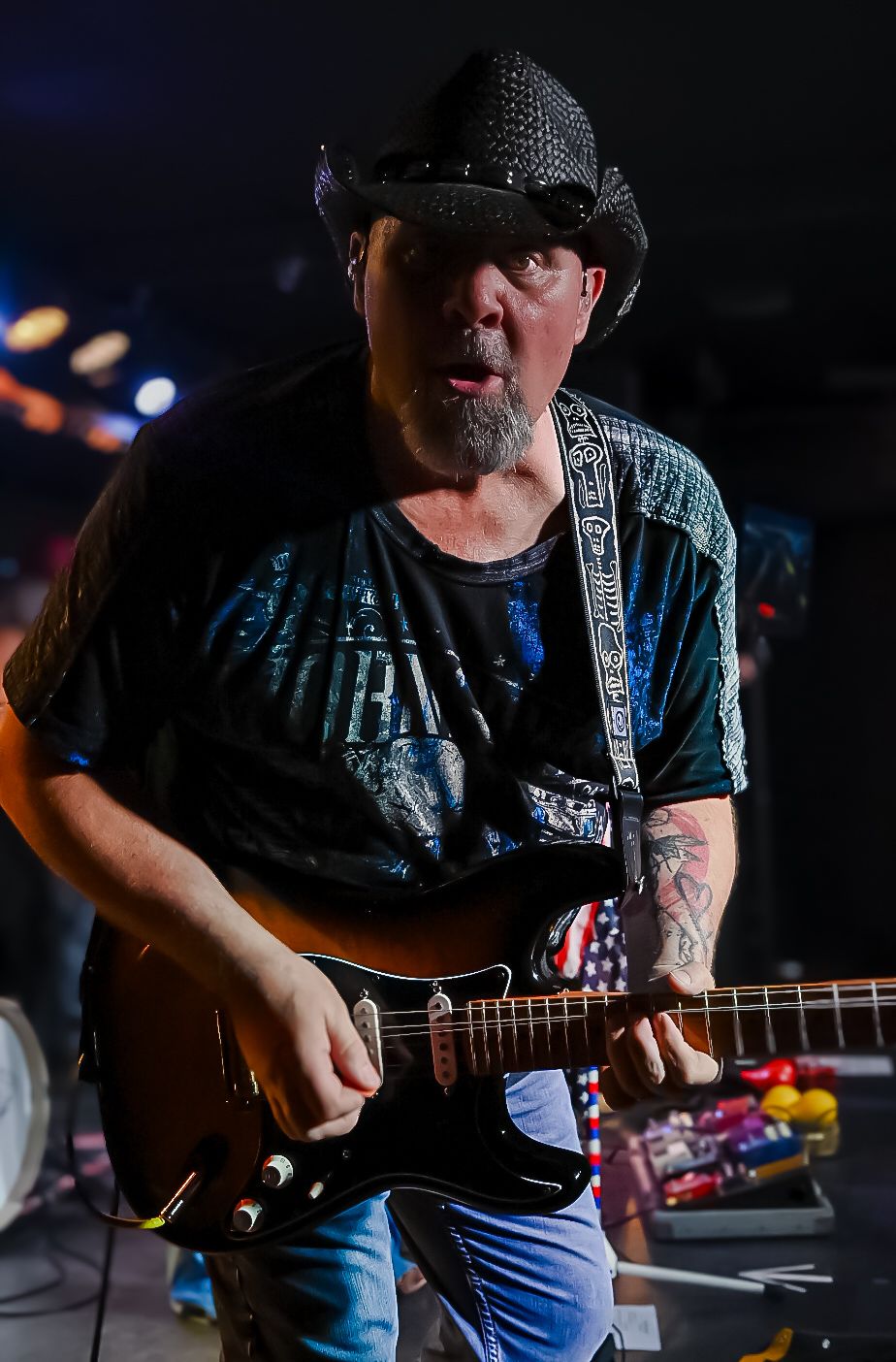 A guitarist in a black cowboy hat performs on stage with dramatic lighting.
