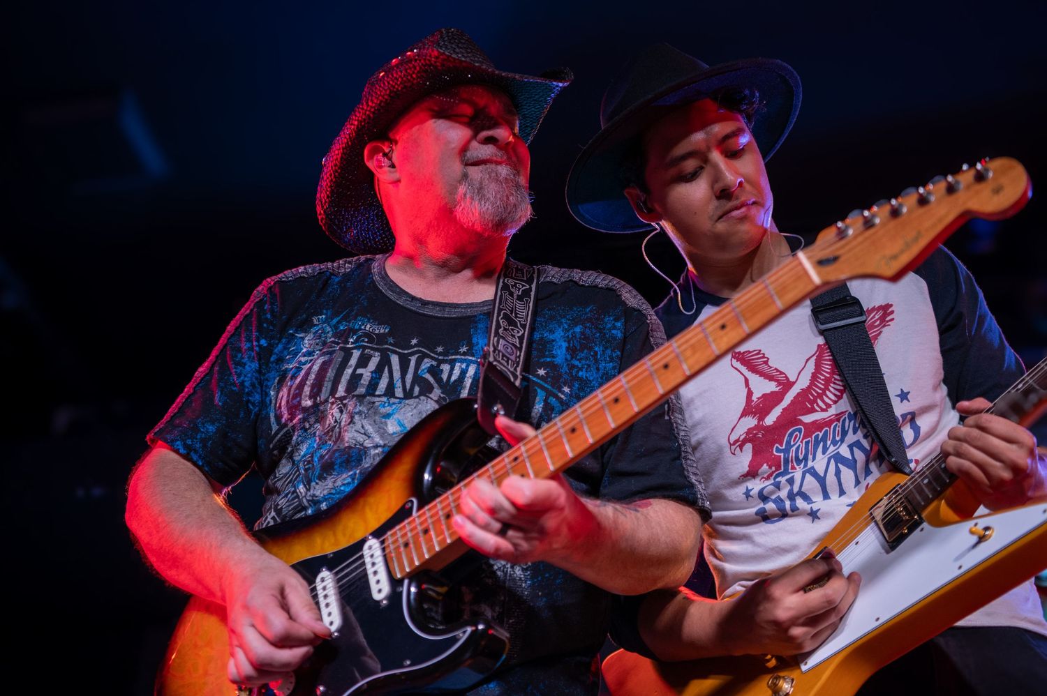 Two guitarists performing together on stage with colorful lighting effects.
