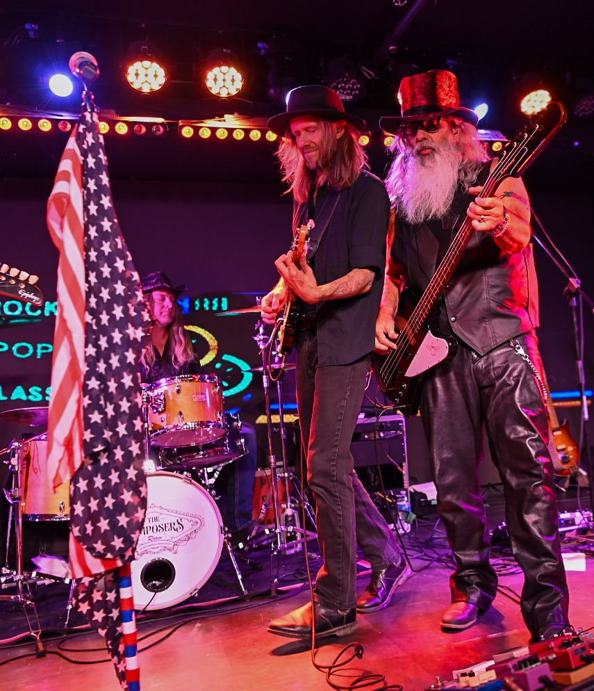 Band members performing on stage with American flag and concert lighting.