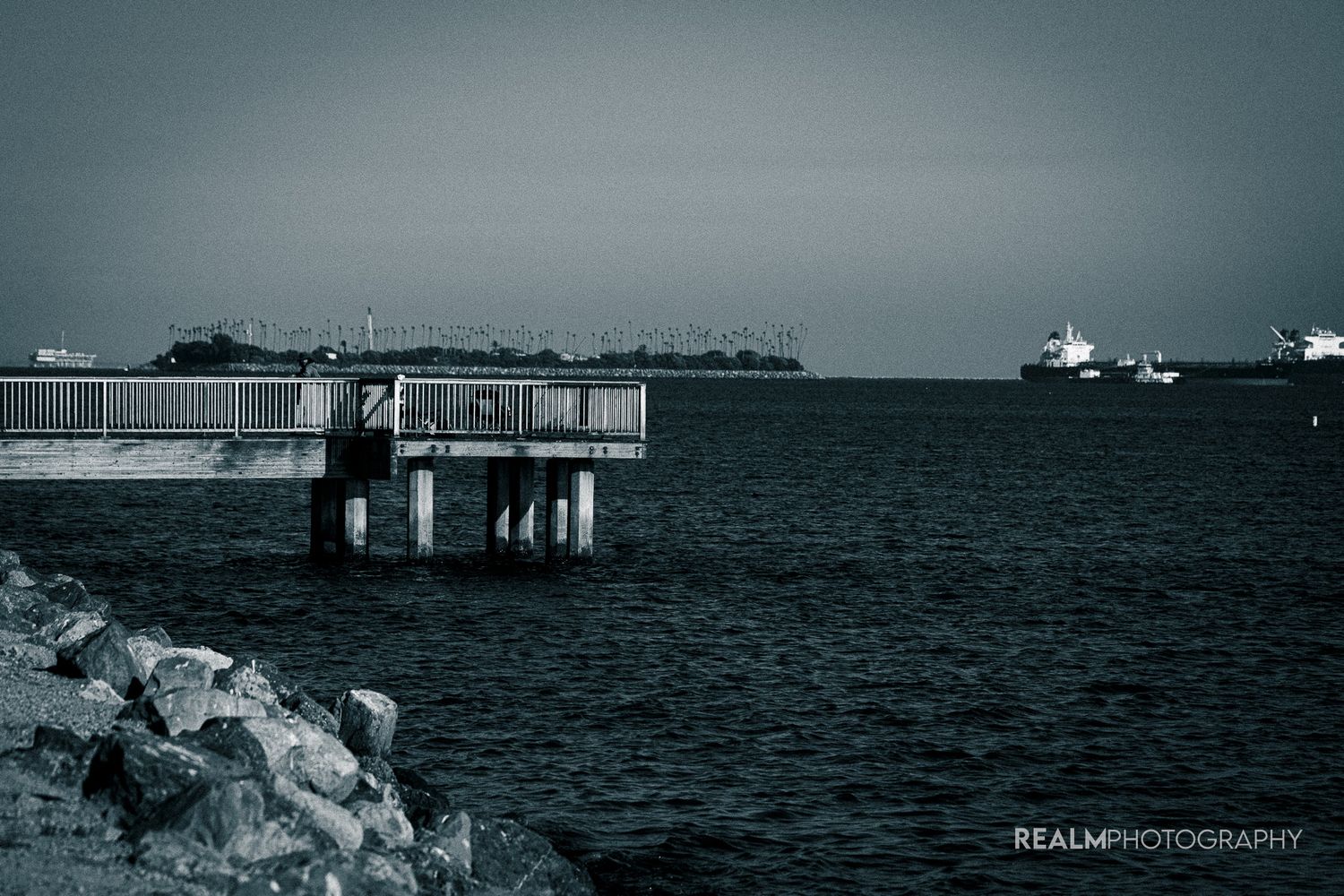 Industrial pier structure extends into dark ocean with ships visible on horizon.