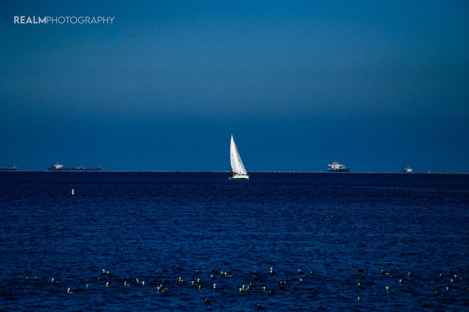 White sailboat on deep blue ocean water against distant horizon.