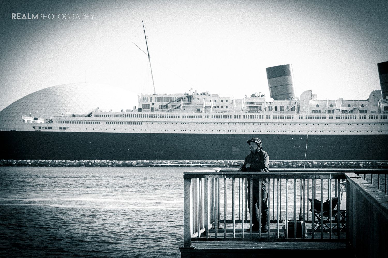 Historic cruise ship docked at pier with lone observer on viewing platform.