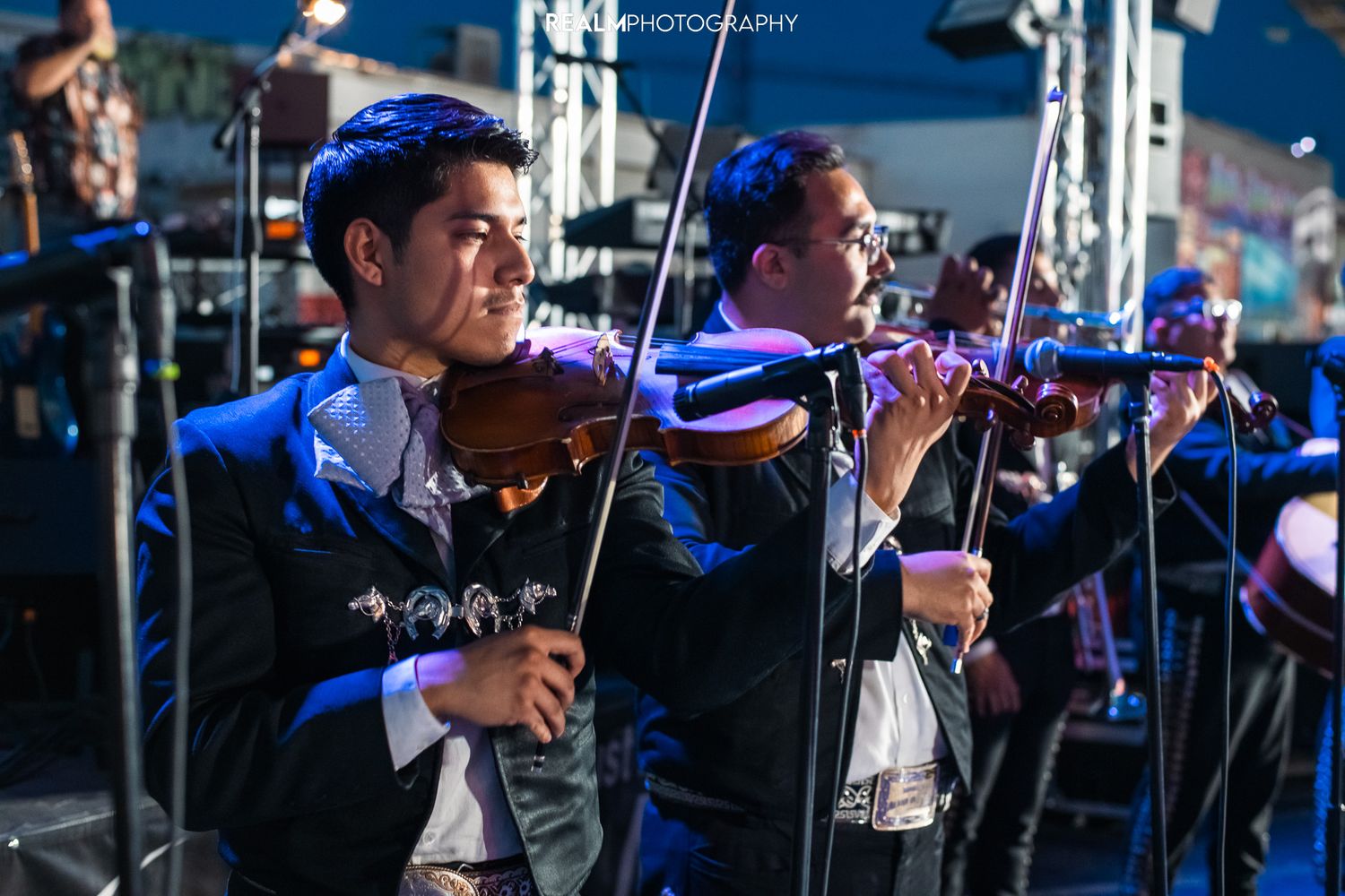 Mariachi violinists performing on stage under blue lighting at night.