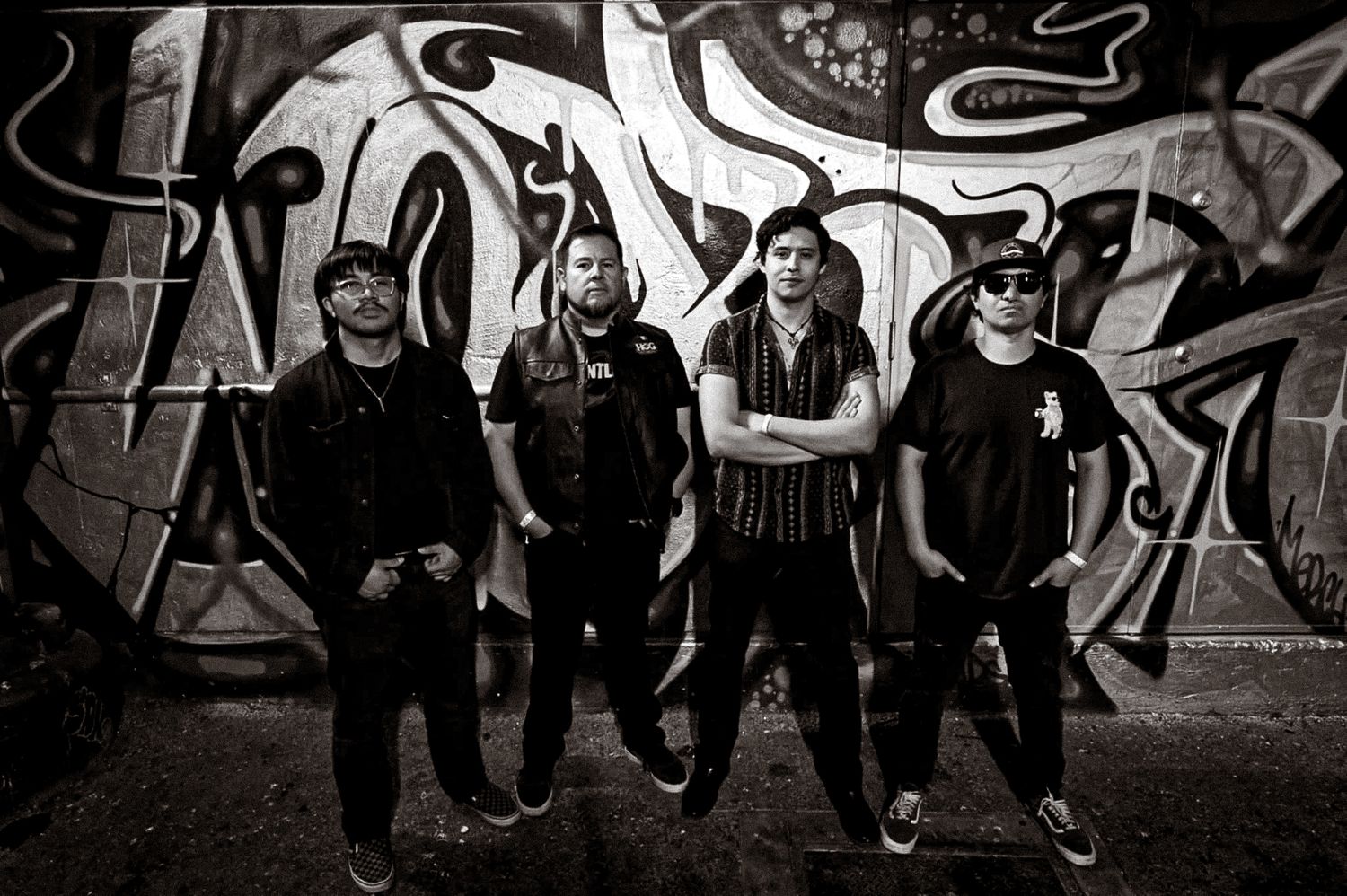 Group of breakdancers performing dynamic moves against a graffiti wall backdrop in black and white.