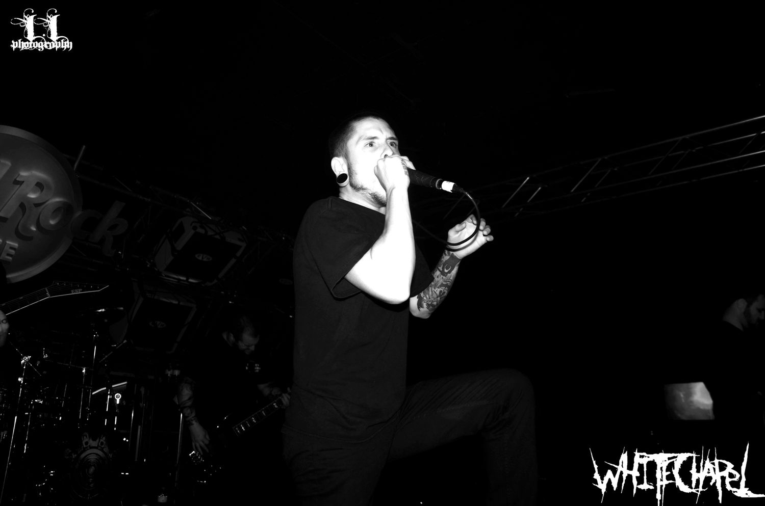 Performer in black sings passionately on stage during dark concert performance.