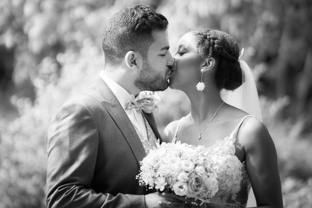 Photo en noir et blanc de jeunes mariés partageant un baiser romantique avec un bouquet de fleurs blanches.