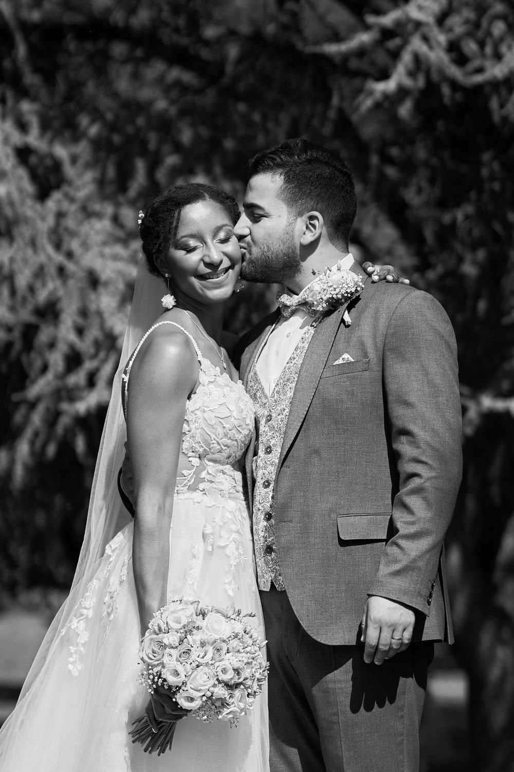 Portrait en noir et blanc de jeunes mariés partageant un moment intime avec la mariée tenant un bouquet blanc.