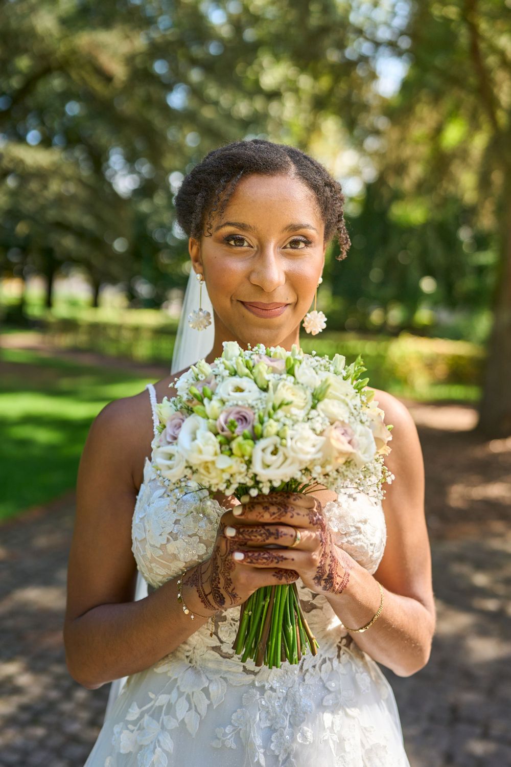 Une belle mariée tient un délicat bouquet blanc et vert dans un cadre de jardin ensoleillé.