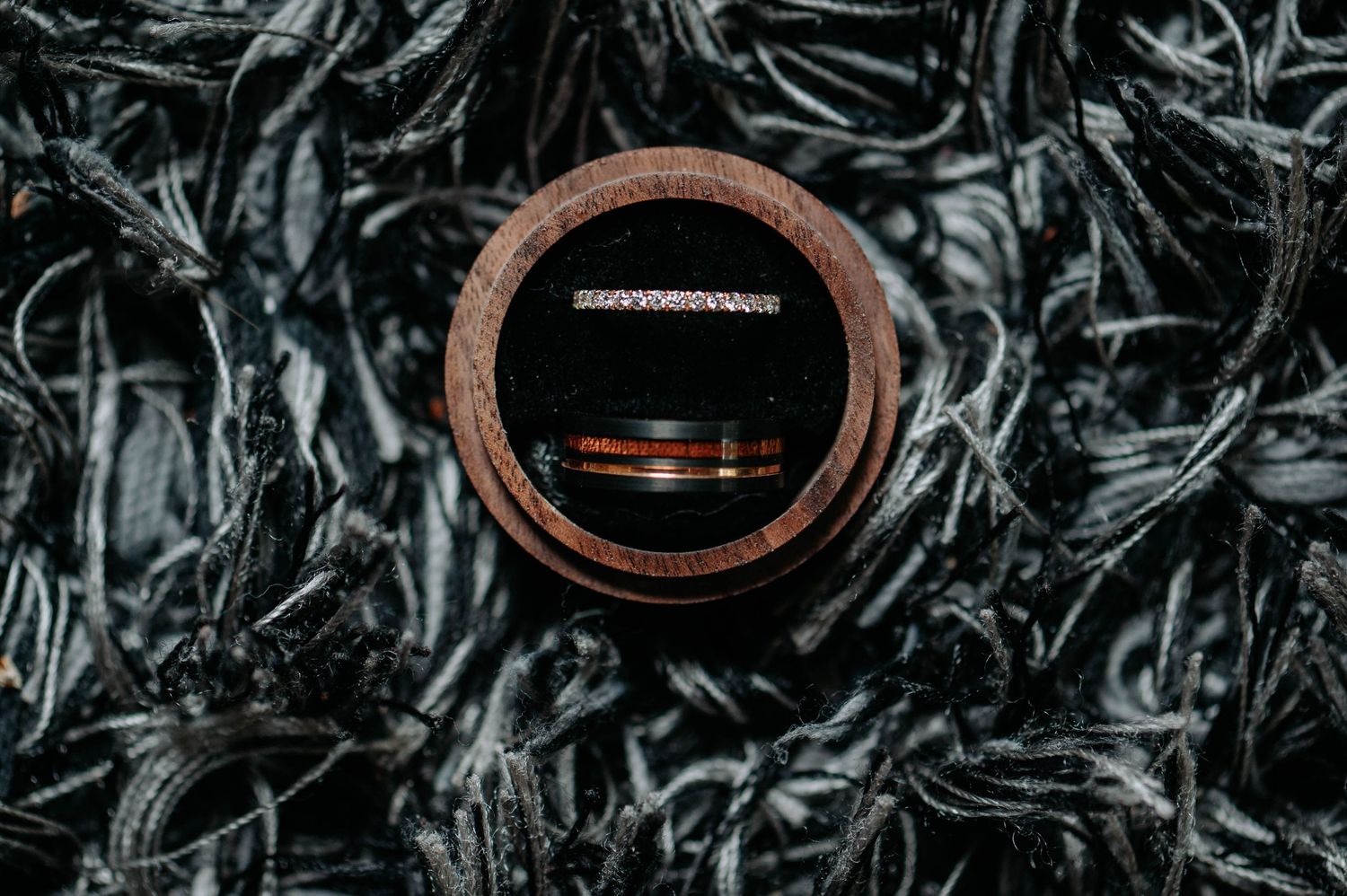 Wedding rings displayed in a wooden box against a dark textured background.
