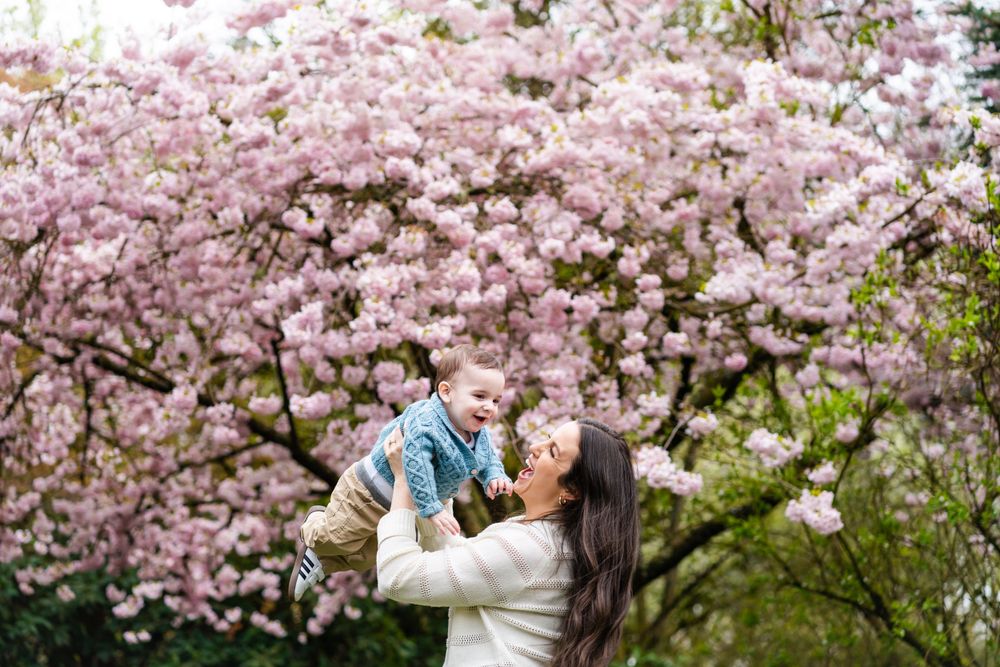 Mom throwing baby in the air in front of cherry blossoms.