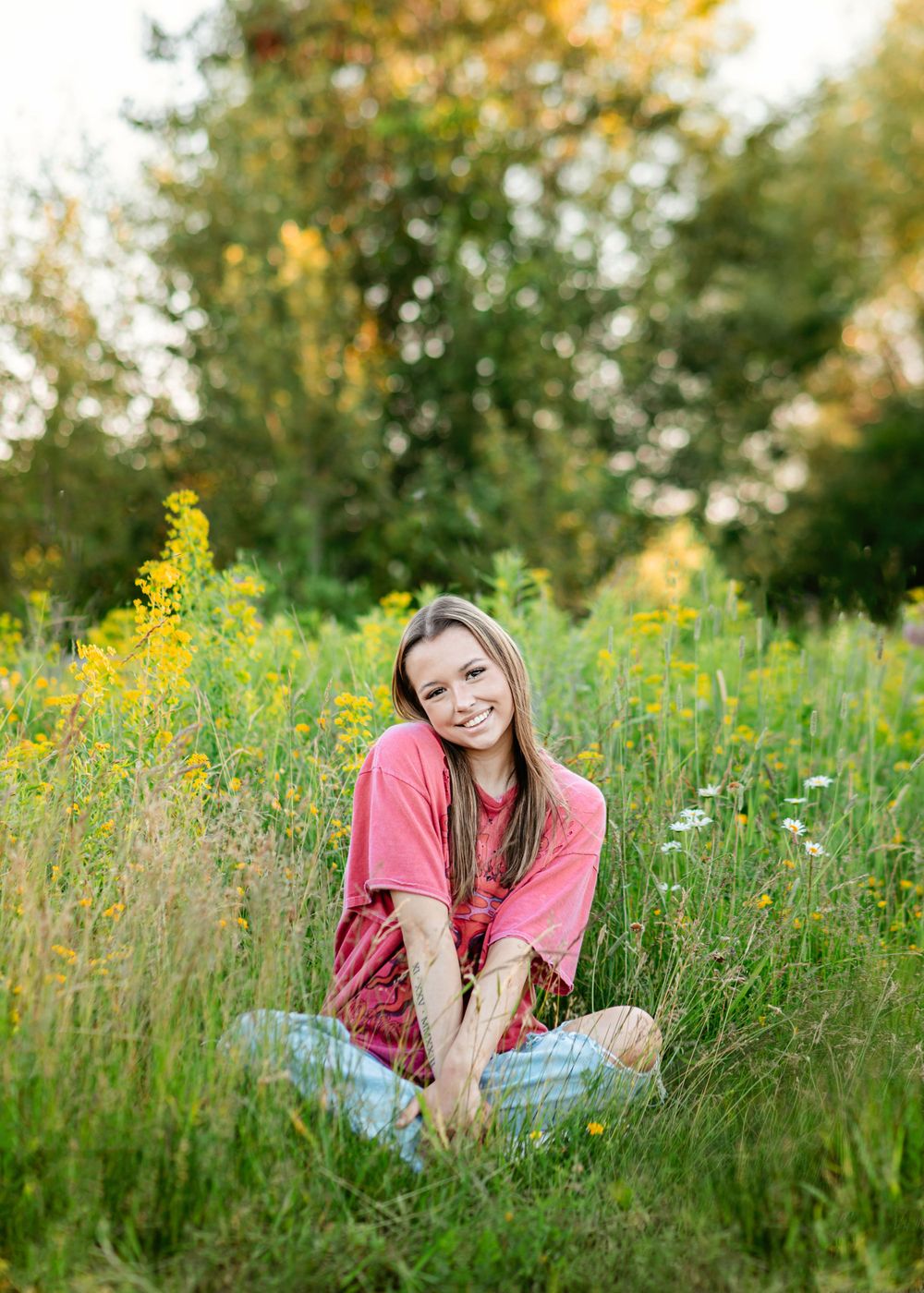 Someone sits in a blooming wildflower meadow wearing a pink shirt and jeans on a sunny summer day.
