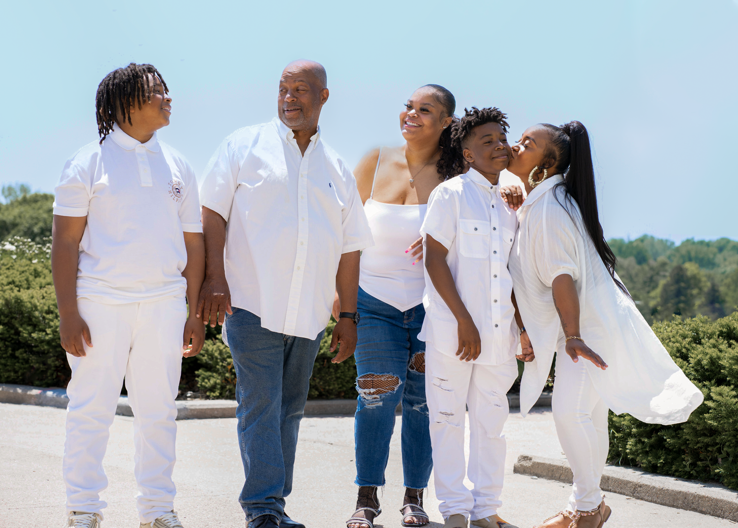 Family wearing coordinated white outfits standing together on outdoor terrace during sunny day.
