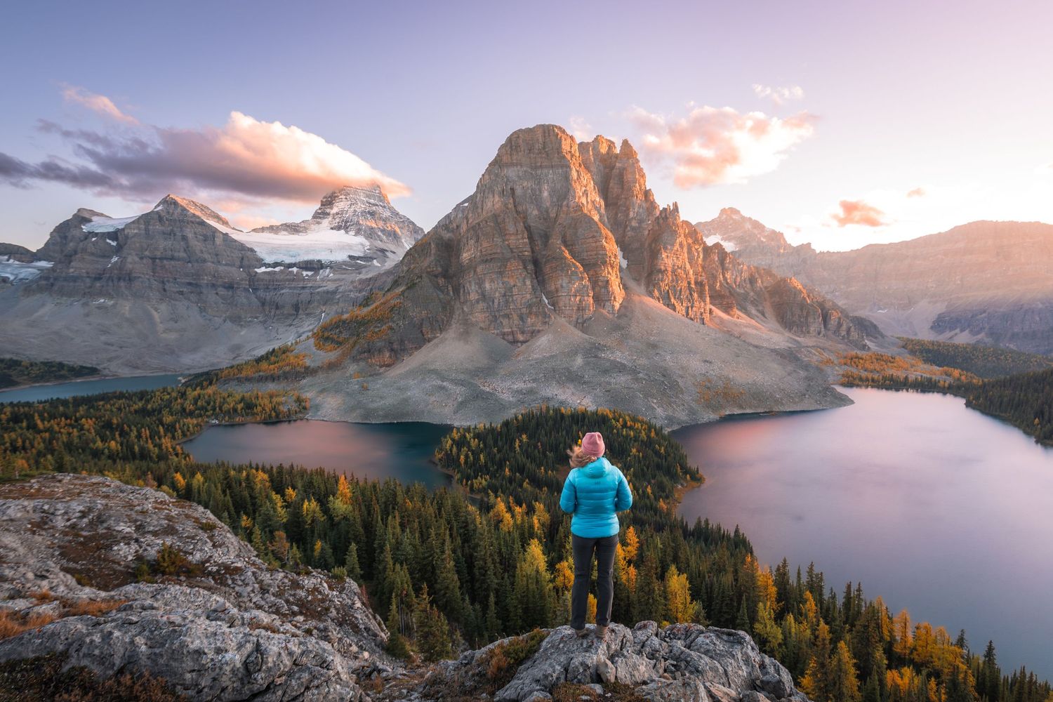Stunning view of Mount Assiniboine reflecting in alpine lake during sunset with person in blue jacket.