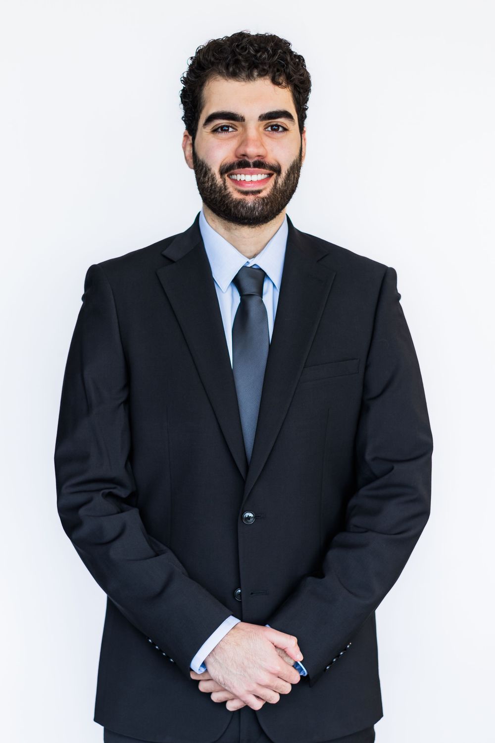 Professional headshot of someone in a dark suit and blue tie smiling against a white background.