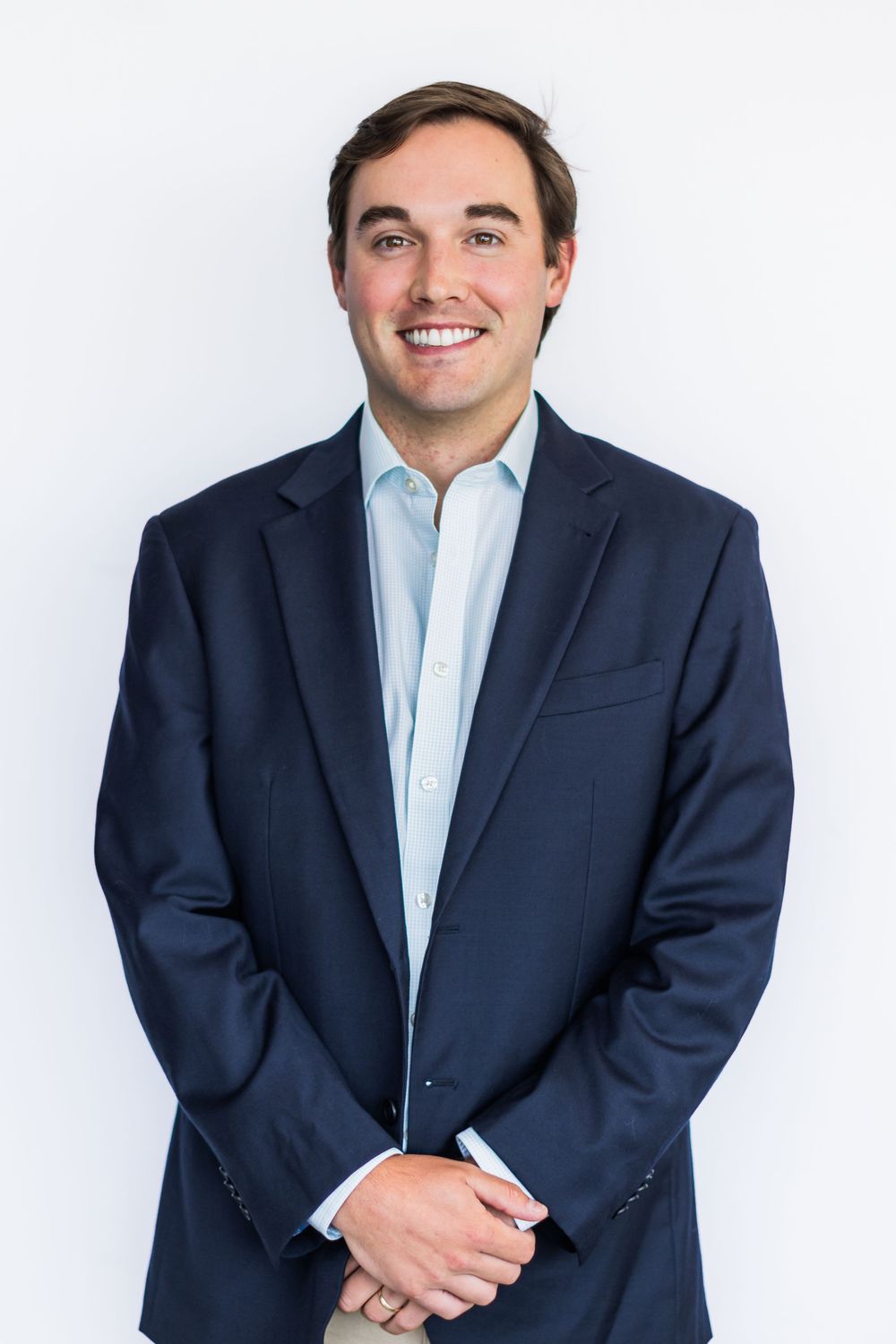 Professional headshot of someone in a navy suit and light blue dress shirt against a white background.