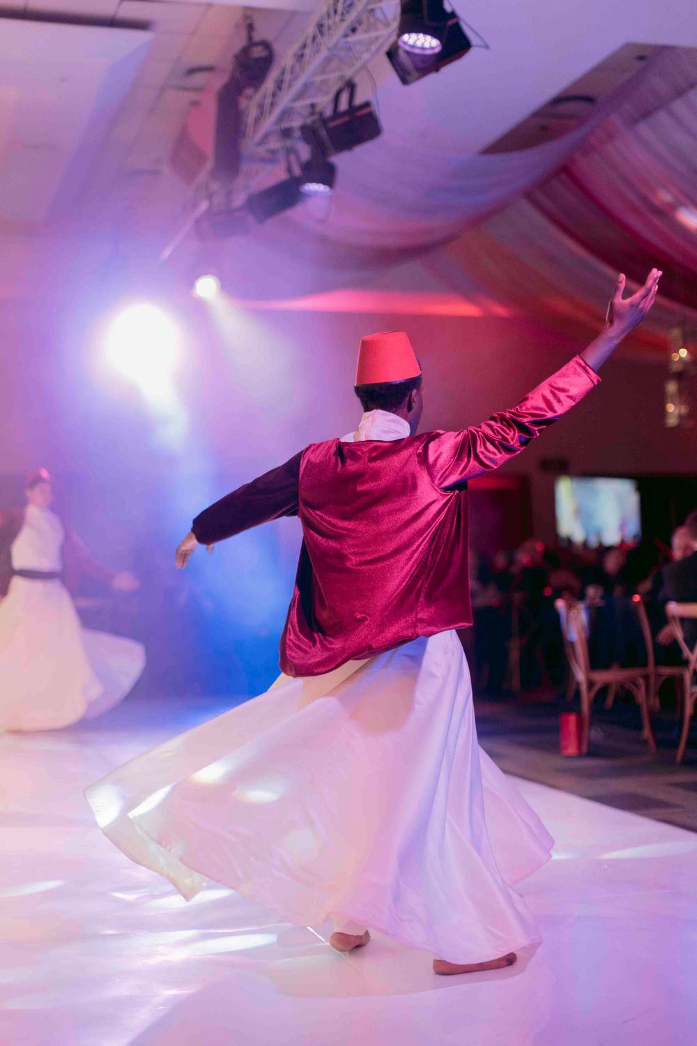 Whirling dervish performer in red fez and white skirt dancing at gala awards evening.