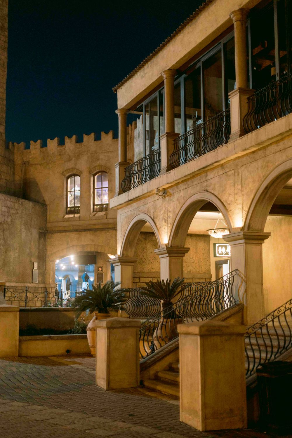 Historic stone building with arched colonnade and wrought iron balcony illuminated at night.