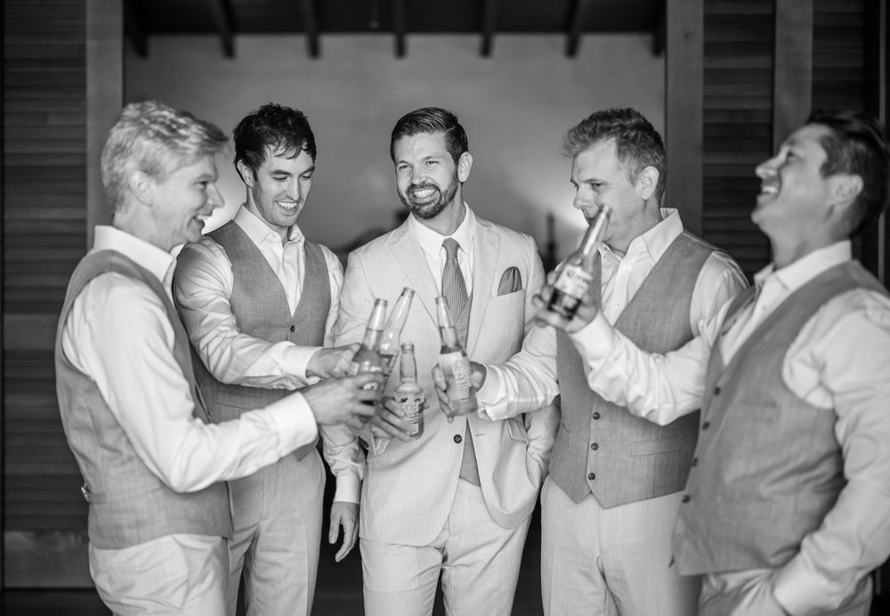 Groomsmen sharing drinks and laughs in black and white photography.