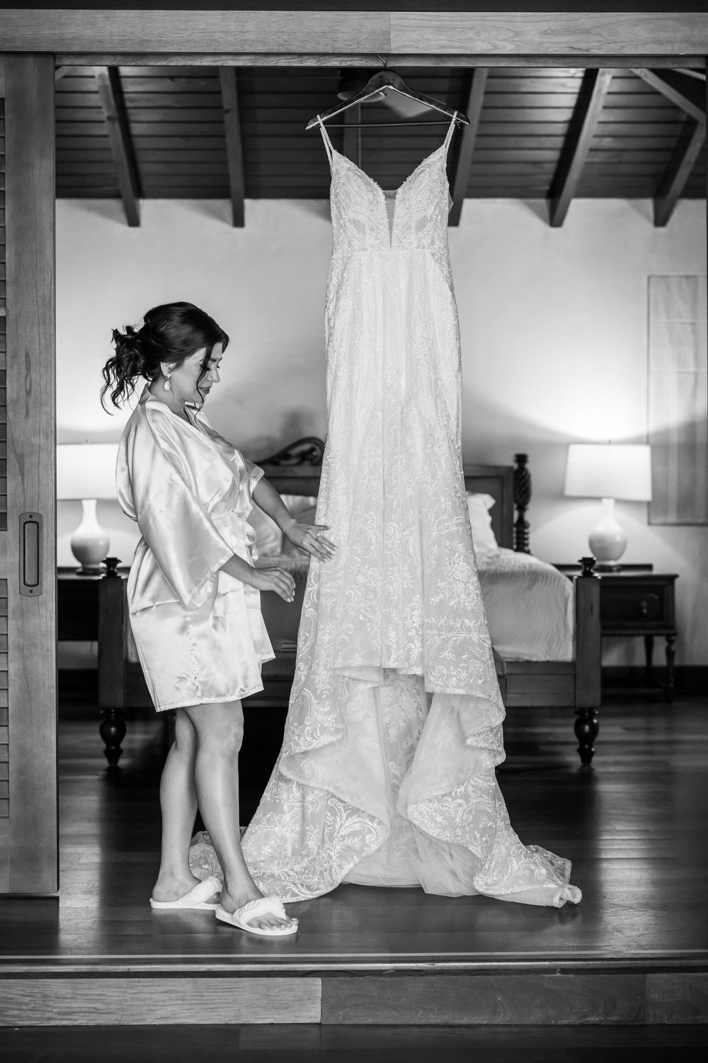 Black and white photo of an elegant wedding dress hanging while being admired.