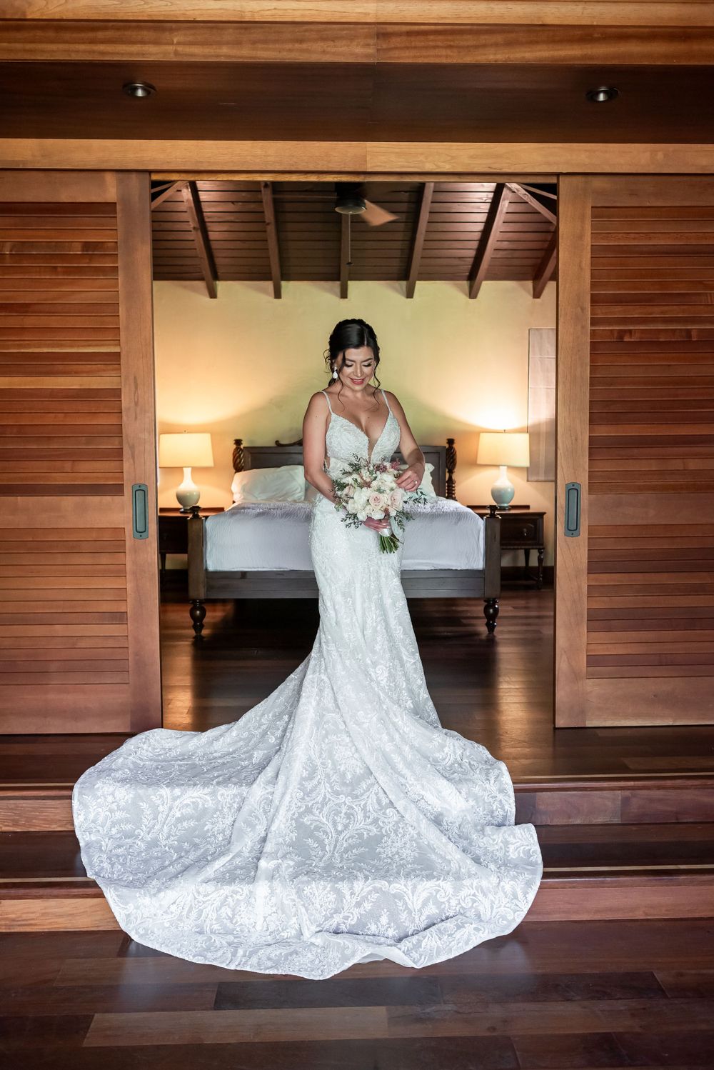 Wedding gown with intricate lace detail spread out on wooden floor with warm lighting.