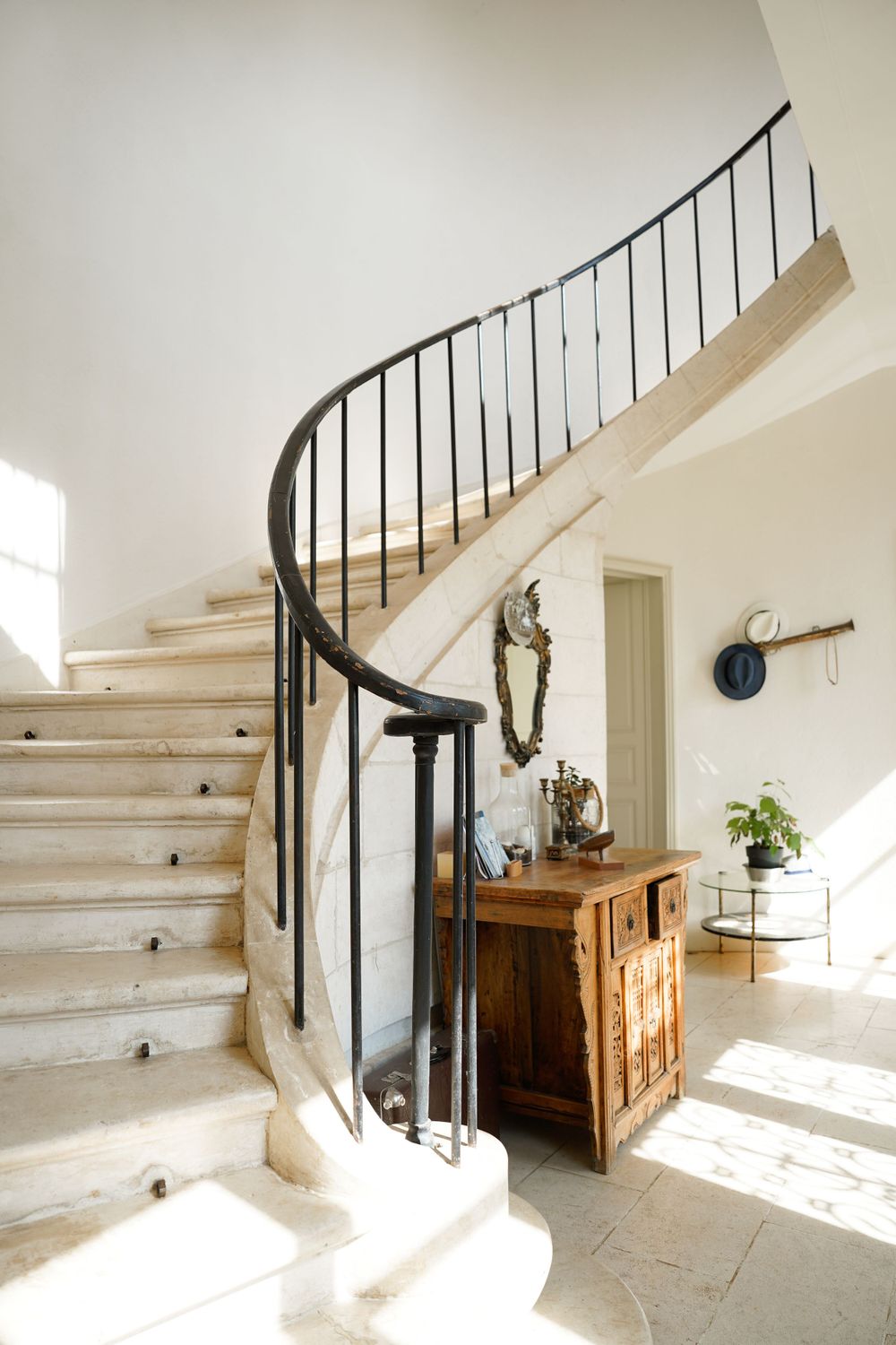 Elegant curved staircase with wrought iron railing in a sunlit French interior.