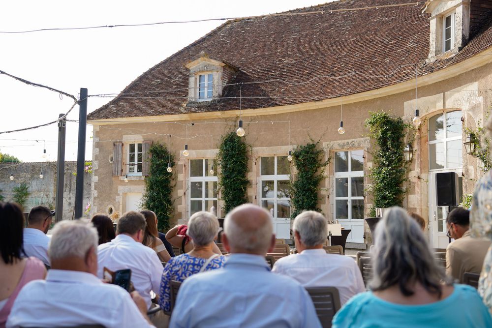 Guests seated in rows of chairs outside a historic stone building with ivy-covered walls for an outdoor event.