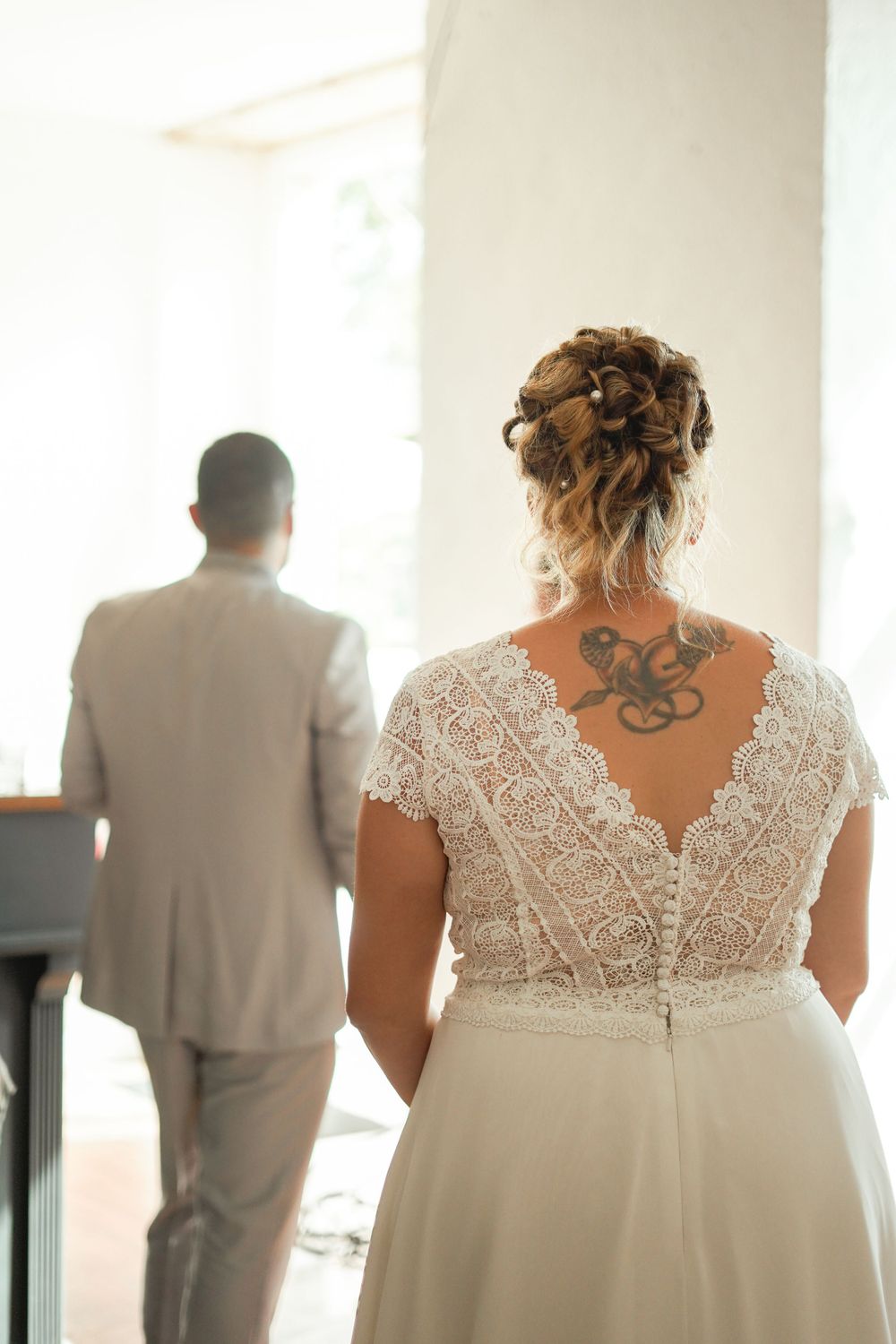 Back view of a bride in a lace wedding dress showing an octopus tattoo with groom in gray suit.