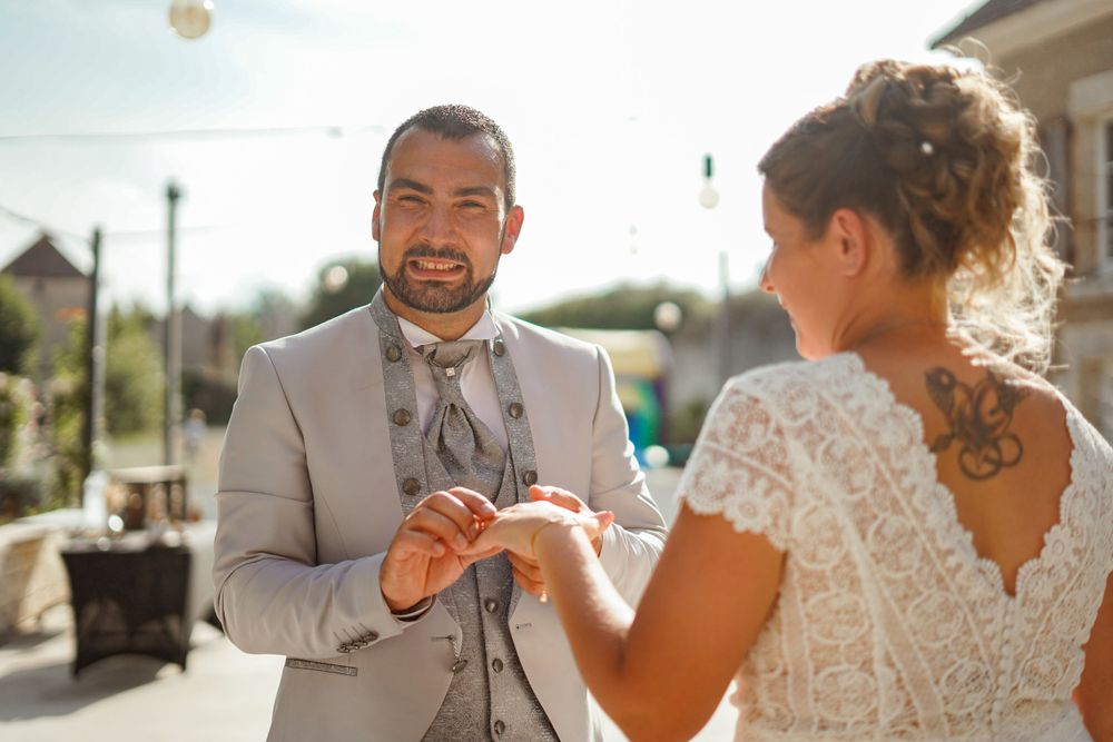 Couple exchanges rings during outdoor wedding ceremony against stone building backdrop.