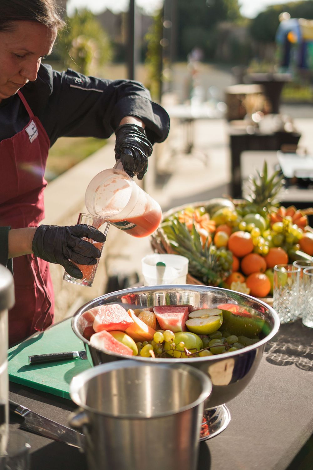 Catering staff member preparing fresh fruit and food at outdoor buffet station.