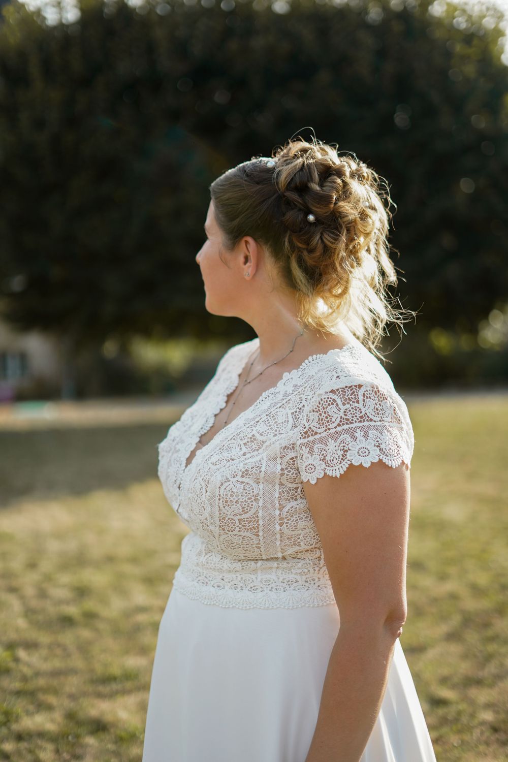 A side profile view showcases an elegant lace wedding dress and romantic updo hairstyle in warm sunlight.