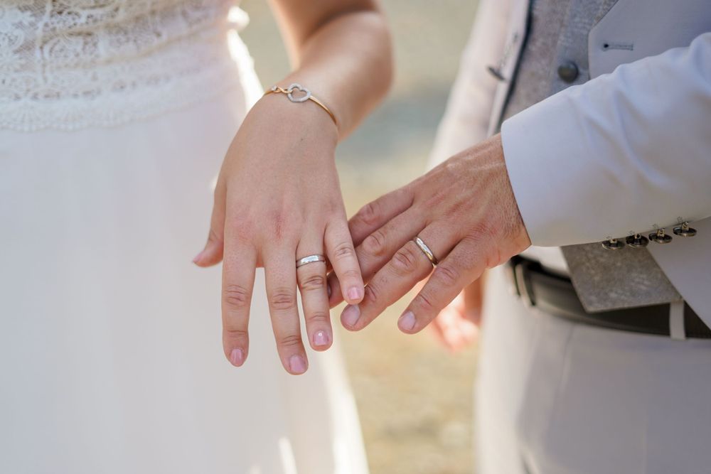 Close-up of wedding rings and hands against white dress fabric in soft natural light.